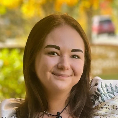 Close-up portrait of a person smiling outdoors with blurred greenery