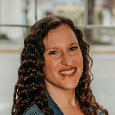 Close-up portrait of an individual with long curly hair smiling indoors